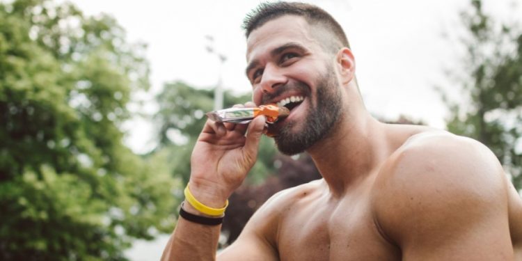 γυμνασμένος άντρας τρώει σνακ τροφές για περισσότερη ενέργεια