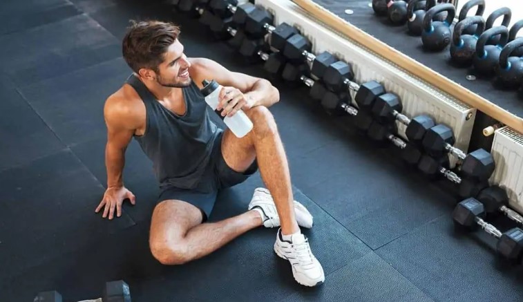 άνδρας πίνει νερό στο γυμναστήριο καθώς κάνει διάλειμμα