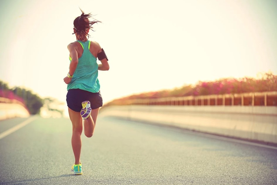 μια γυναίκα τρέχει φορώντας ανοιχτόχρωμα ρούχα μια μέρα με ήλιο και ζέστη φορώντας τα αθλητικά της ρούχα