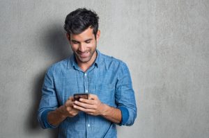 χαμογελαστός άντρας κρατάει κινητό φλερτ μέσω Instagram